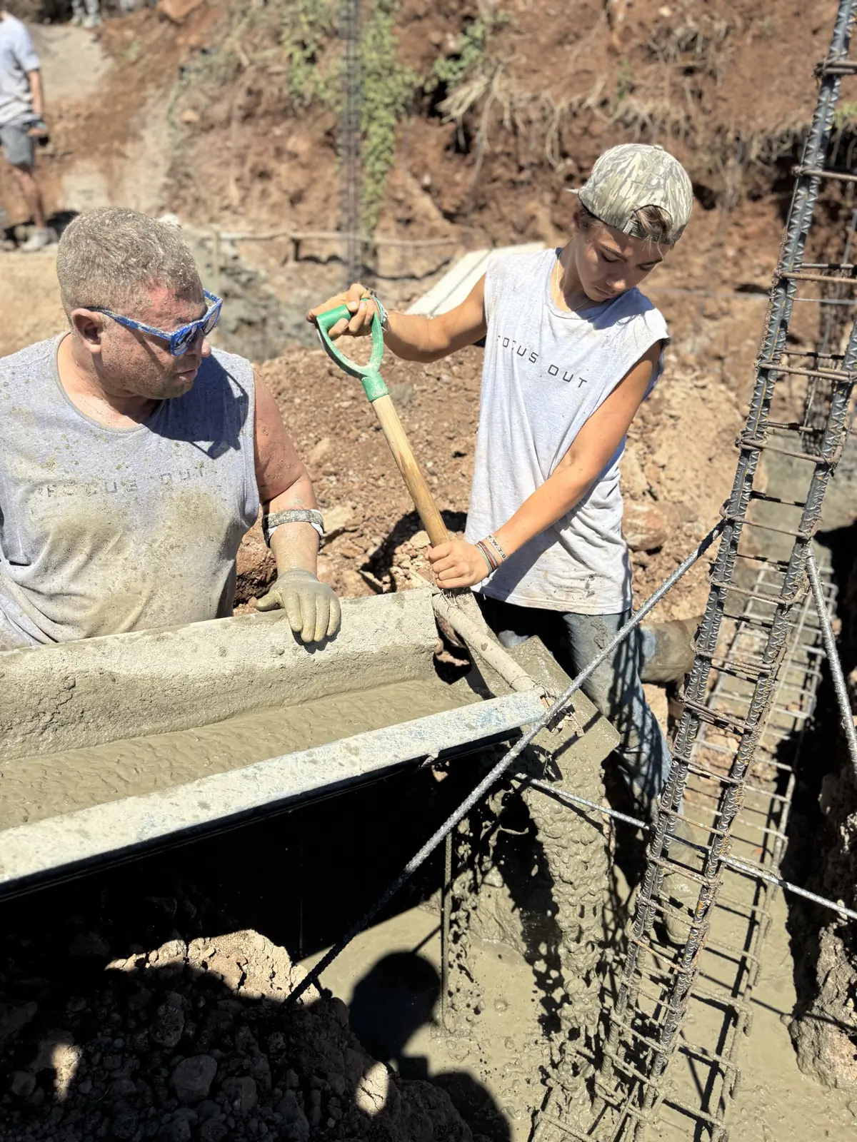 Two men smoothing wet concrete in a foundation trench, one holding a shovel.